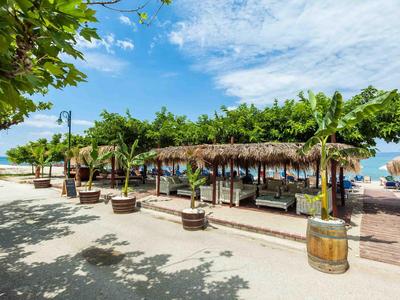 Sonnige Strandpromenade mit Schatten spendendem Pavillon und tropischer Vegetation.