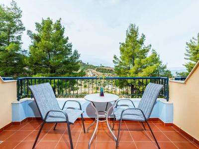Balcón con dos sillas y mesa pequeña, rodeado de árboles y montañas al fondo.