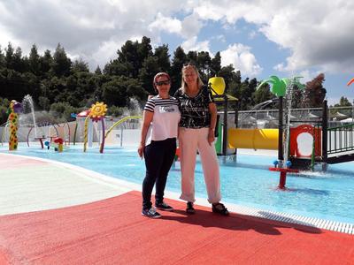 Dos mujeres están juntas en un colorido parque acuático con toboganes y aspersores.