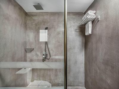 Cuarto de ducha moderno en gris en hotel con mampara de vidrio, toallero y ducha de lluvia.