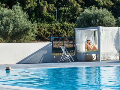 Persona sentada relajándose en una cama cubierta junto a una piscina en un entorno tranquilo.