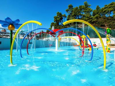 Área de juegos acuáticos colorida con fuentes en una piscina soleada.
