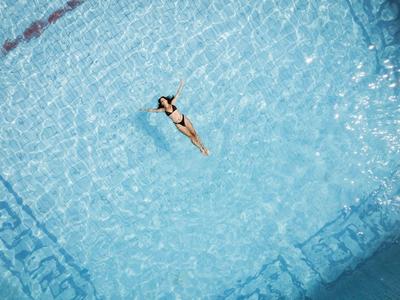 Person schwimmt in klarem blauen Wasser eines Pools mit gemustertem Boden.
