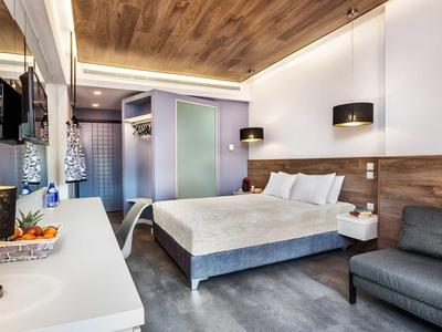 Habitación de hotel moderna con cama doble, sofá, TV y techo de madera en ambiente luminoso.