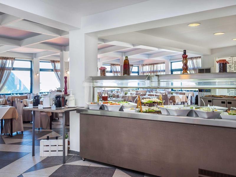 Restaurante luminoso con buffet, mesas preparadas y grandes ventanas con vista al mar.