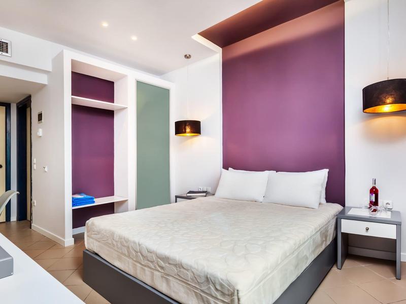 Habitación de hotel moderna con cama doble, pared púrpura y mesitas con luces.