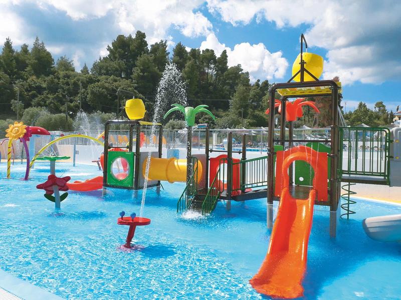 Parque acuático colorido con tobogán y fuente en la piscina bajo cielo nublado.