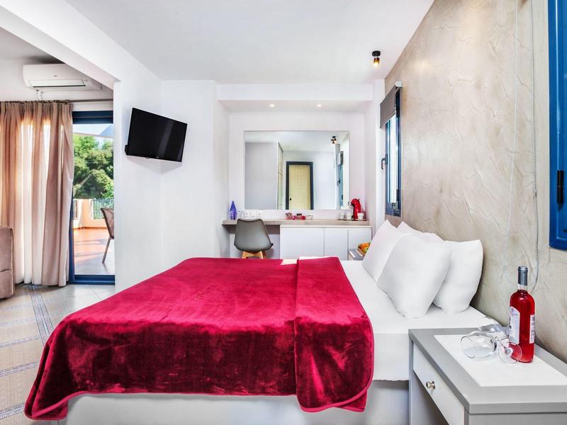 Habitación de hotel moderna con colcha roja, mobiliario blanco y acceso al balcón.