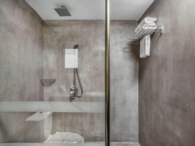 Cuarto de ducha moderno en gris en hotel con mampara de vidrio, toallero y ducha de lluvia.