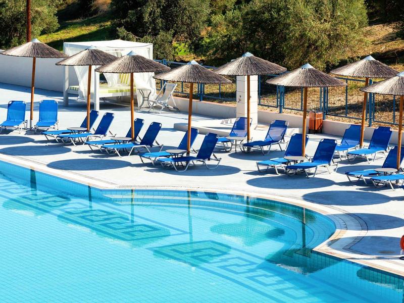 Área de ocio con varias tumbonas azules y sombrillas junto a una piscina en un hotel.