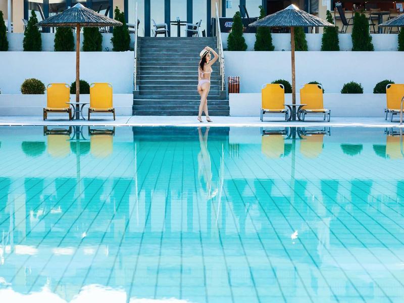 Piscina con agua clara y tumbonas amarillas frente a escaleras y sombrillas.