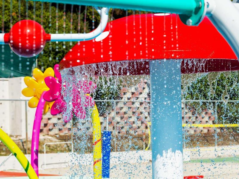 Juegos de agua coloridos con elementos rojos, azules y amarillos en una zona de piscina exterior.