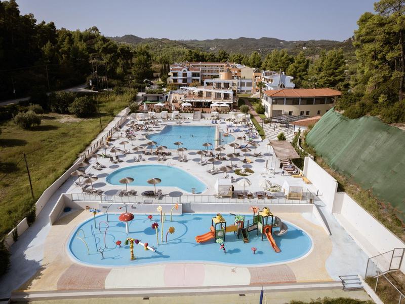 Amplia área de piscina del hotel con tumbonas, piscina infantil y parque acuático, rodeada de naturaleza.