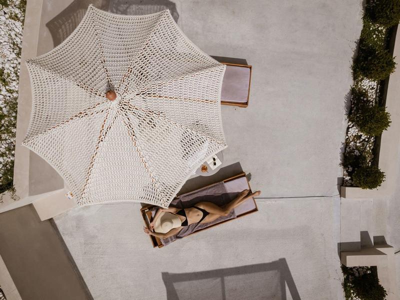 Una persona se relaja en una tumbona bajo una gran sombrilla en una terraza.