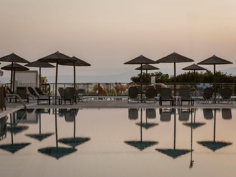 Piscina tranquila al atardecer con tumbonas y sombrillas en la playa.