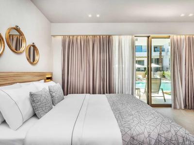 Chambre d'hôtel moderne avec grand lit, rideaux gris et accès au balcon.