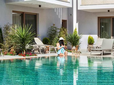 Kobieta siedzi na brzegu basenu w hotelowym ogrodzie z leżakami i roślinami.