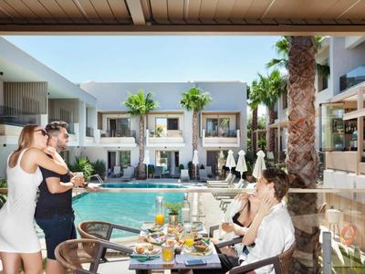 Taras hotelowy z gośćmi siedzącymi przy nakrytym stole z widokiem na basen, śmiejący się.