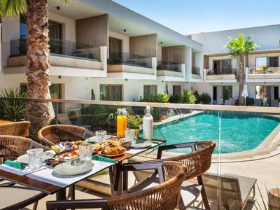 Piscina moderna dell'hotel con tavolo da pranzo e sedie all'aperto, circondata da palme.