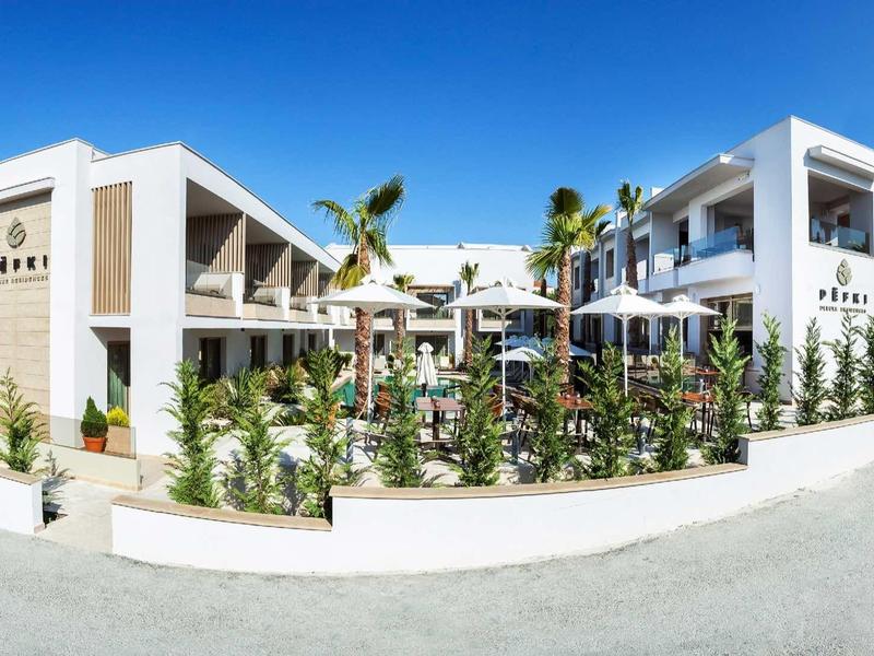 Nowoczesny hotel z białą fasadą, przestrzenią na zewnątrz i palmami pod czystym niebem.