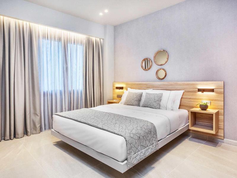 Nowoczesny pokój hotelowy z dużym łóżkiem, szarymi zasłonami i dekoracyjnymi panelami ściennymi.