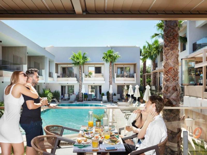 Taras hotelowy z gośćmi siedzącymi przy nakrytym stole z widokiem na basen, śmiejący się.