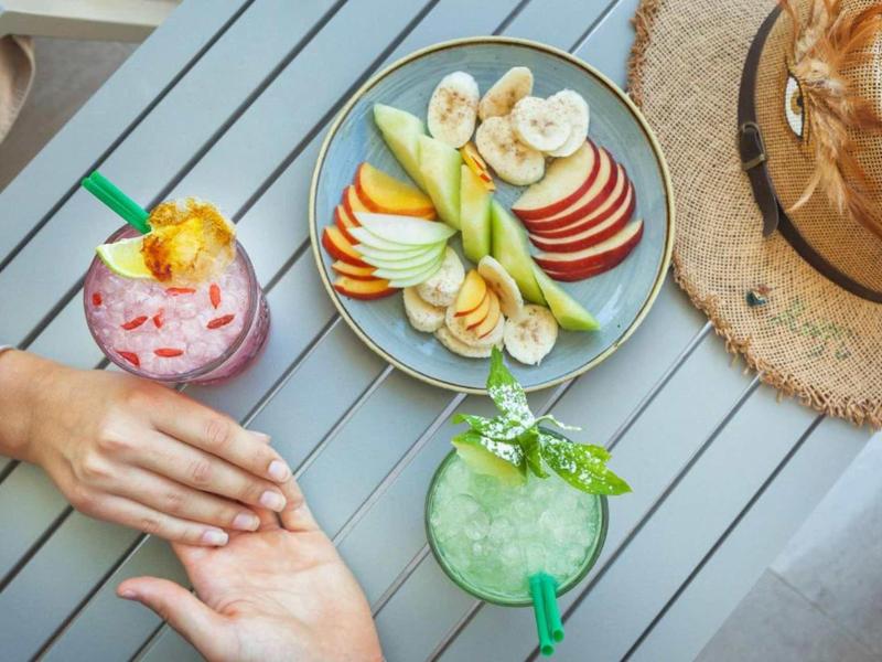 Dwa napoje i talerz owoców na szarym stole, dłonie się dotykają.