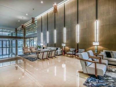 Moderne Hotellobby mit hellen Sesseln, Teppichen, hoher Decke und vertikalen Wandlampen.