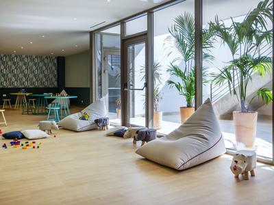 Heller Raum mit großen Fenstern, weich gepolsterten Sitzsäcken und großen Topfpflanzen.