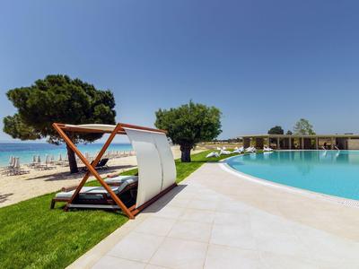 Sonnenliege mit weißem Stoff neben Pool, Blick auf Strand und Blaues Meer unter klarem Himmel