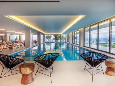 Moderner Innenpool mit schwarzen Stühlen, Holzhockern und Panoramafenstern mit Meerblick.