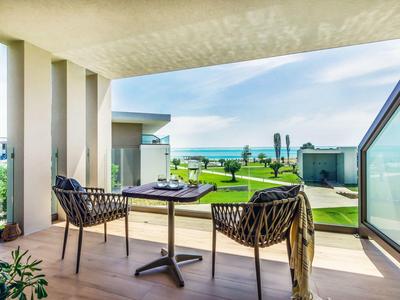 Moderner Balkon mit Tisch, zwei Stühlen und Meerblick bei klarem Himmel.