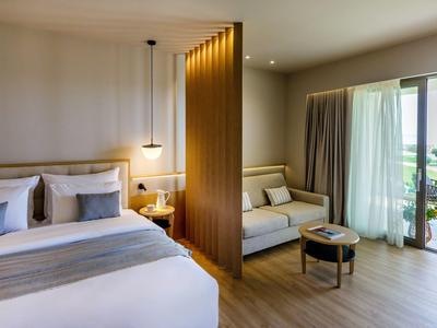 Modernes Hotelzimmer mit Doppelbett, Trennwand, Sitzbereich und Balkon mit Aussicht.