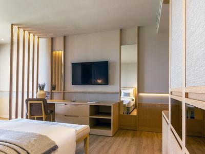 Helles, modernes Schlafzimmer mit Holzdetails, Flachbildschirm, Stuhl und minimalistischer Dekoration.