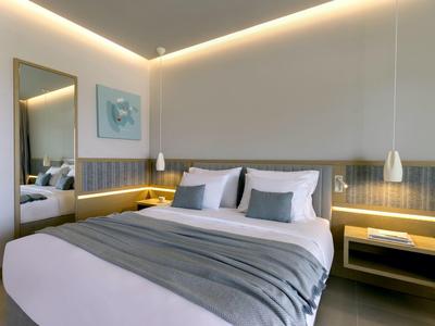 Modernes Schlafzimmer mit rundem Bett, grauer Bettwäsche, Wandspiegel und warmweißer Beleuchtung.