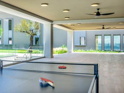 Überdachter Bereich mit Tischtennisplatte und Blick auf einen Garten und Gebäude im Hintergrund.