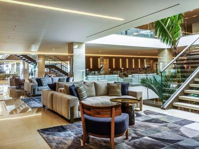 Großer moderner Wohnbereich mit Sofas, Sesseln, Teppich und Treppe mit Glasgeländer.