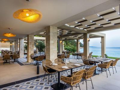 Offener Restaurantbereich mit Stühlen und Tischen mit Blick auf das Meer.