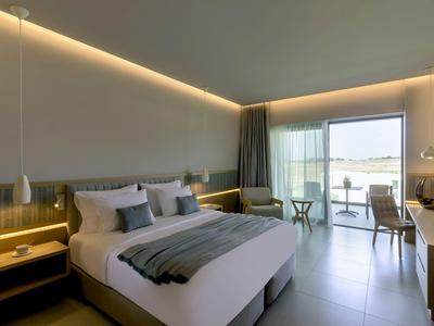 Modernes Hotelzimmer mit großem Bett, indirekter Beleuchtung und Terrasse mit Blick aufs Wasser.