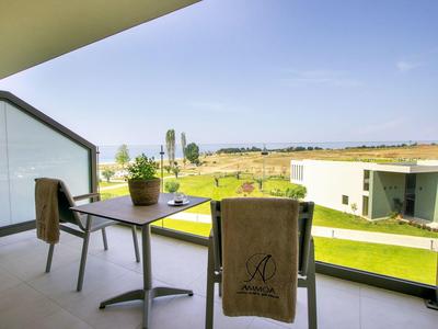 Balkon mit Tisch, zwei Stühlen, zwei braunen Handtüchern und Blick auf grünes Feld und Gebäude.