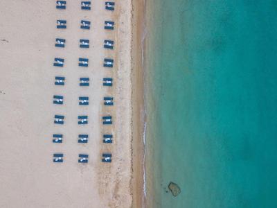 Luftaufnahme eines Strandes mit Reihen von blauen Sonnenliegen und türkisfarbenem Meer.