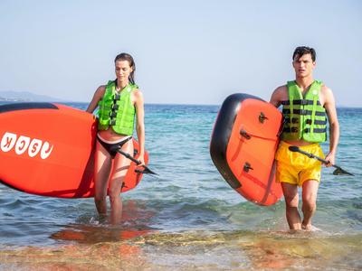 Zwei Personen mit Schwimmwesten tragen Stand-up-Paddle-Boards am Strand ins Wasser.