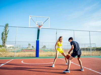 Zwei Personen spielen Basketball auf einem Außenplatz bei klarem Himmel.