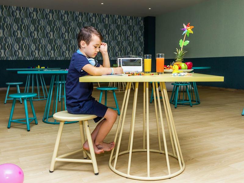 Ein Junge sitzt barfuß an einem runden Tisch mit Metallgestell, vor ihm steht ein Müsli und Orangensaft.