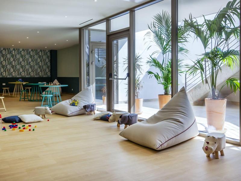 Heller Raum mit großen Fenstern, weich gepolsterten Sitzsäcken und großen Topfpflanzen.