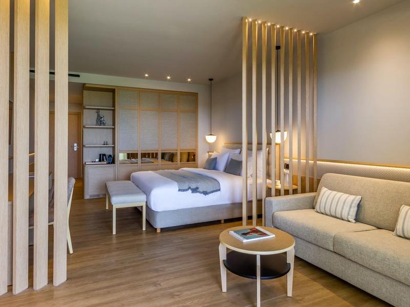 Modern eingerichtetes Hotelzimmer mit Doppelbett, Sofa, Holzboden und stilvollen Holztrennwänden.