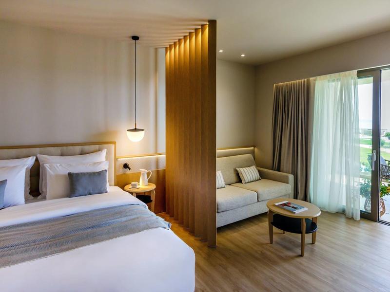 Modernes Hotelzimmer mit Holzboden, Doppelbett, Sofa, Holzwandteiler und Balkon mit Blick.