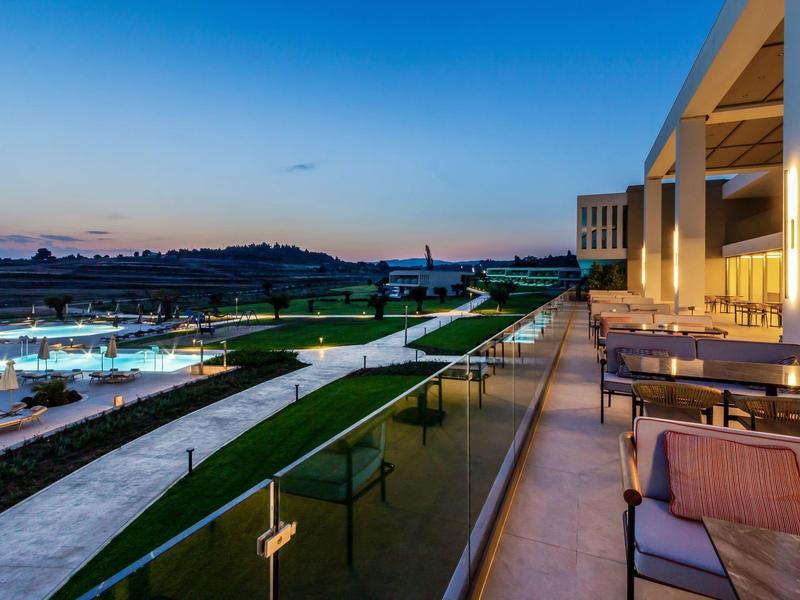 Moderner Außenbereich mit Sitzgelegenheiten, beleuchteten Wegen und Schwimmbecken bei Sonnenuntergang.