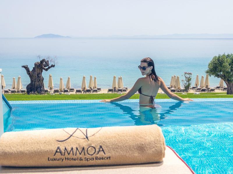Frau im Bikini entspannt sich am Pool eines Resorts mit Blick auf Meer und Liegestühle.