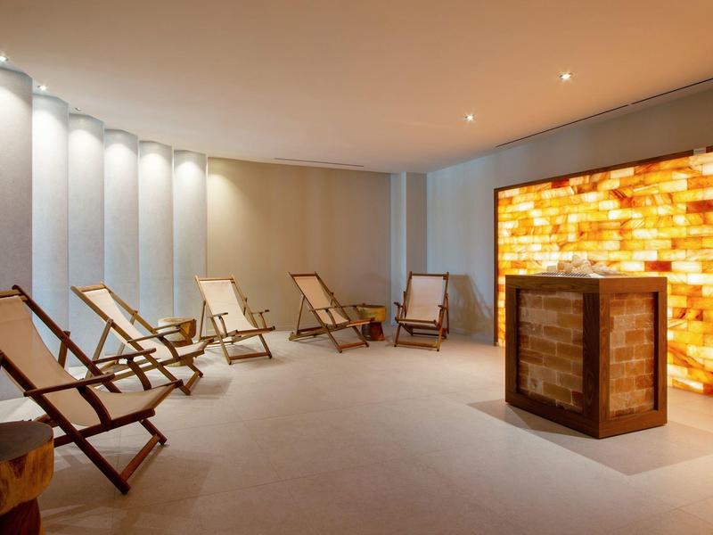 Heller Ruheraum mit Holzliegestühlen und salzsteinverkleideter Wand mit Beleuchtung.